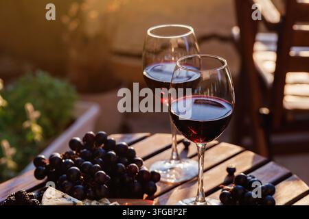 Due bicchieri di vino rosso con uva e formaggio su un tavolo di legno Foto Stock