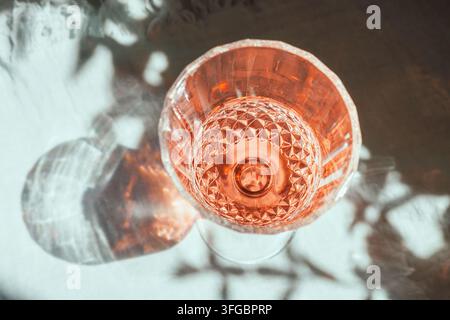 Vetro di cristallo con vino frizzante rosa in posa piatta alla luce naturale del sole Foto Stock