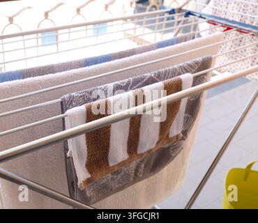 Biancheria bagnata che si asciuga su una rastrelliera di metallo per il bucato posizionata sul pavimento del balcone. Foto Stock