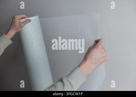 Mani maschili che tengono un rotolo di rete di gesso bianca per lavori di preparazione e pittura. Foto Stock
