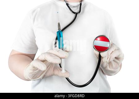 Un medico con guanti tiene una siringa e uno stetoscopio con la bandiera austriaca, su sfondo bianco Foto Stock