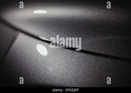 Dettaglio ravvicinato delle curve strutturate della carrozzeria metallica con riflessi di luce morbida, design automobilistico in macro e fotografia di superficie. Foto Stock