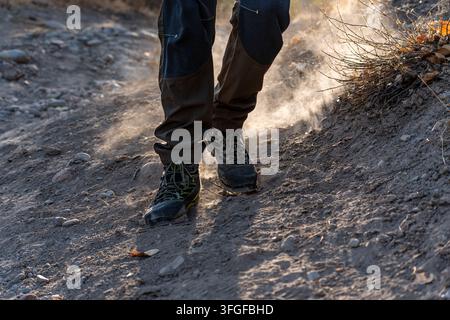 Prima piano ad angolazione bassa dei piedi di un escursionista con scarponi da trekking che camminano su un sentiero polveroso al tramonto. Foto Stock