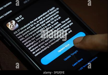 In questa illustrazione fotografica, una persona preme il pulsante "Aggiorna ora" su un iPhone che mostra lo schermo dell'aggiornamento software iOS 27, evidenziando l'ultima novità di Apple Foto Stock