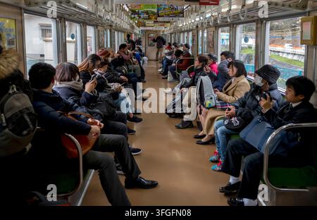 Passeggeri giapponesi che viaggiano a bordo di un treno locale per pendolari, seduti tranquillamente all'interno, guardano i telefoni cellulari e si occupano dei fatti propri in Giappone. Foto Stock