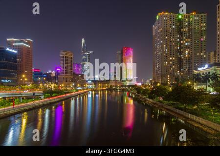 Luci colorate della città, grattacieli e tracce di traffico si riflettono in un canale in un paesaggio urbano notturno denso. Foto Stock