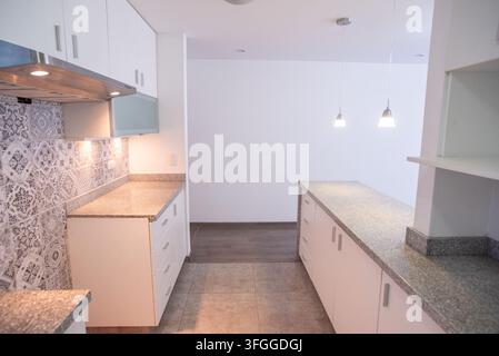 Spazio cucina moderno: Una cucina pulita e contemporanea con mobili bianchi, piani di lavoro in granito e un elegante rivestimento posteriore, pronta per uno chef domestico Foto Stock