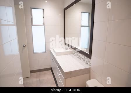 Mobile da bagno moderno: Un mobile da bagno pulito e minimalista con un lavabo a vasca, un piano di lavoro elegante e un grande specchio rettangolare Foto Stock