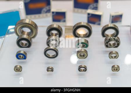 Prima vista di varie dimensioni di cuscinetti a sfere industriali in acciaio disposti su un espositore con confezioni sfocate sullo sfondo. Foto Stock