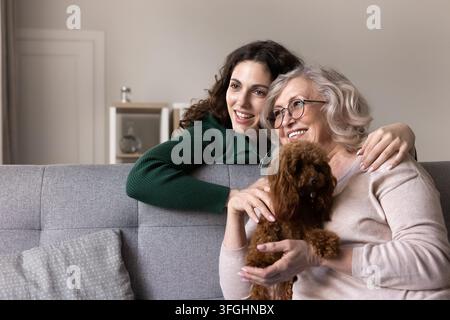 Donna che abbraccia la madre anziana seduta su un divano con un cagnolino Foto Stock