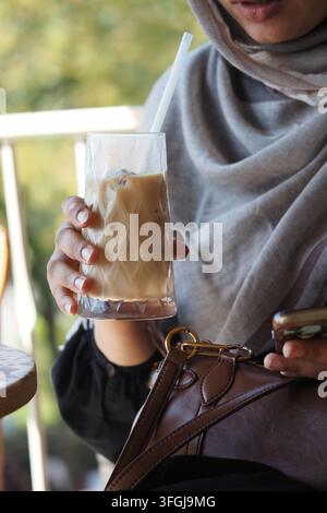 Donna che tiene un bicchiere di caffè freddo mentre usa il telefono in un caffè Foto Stock
