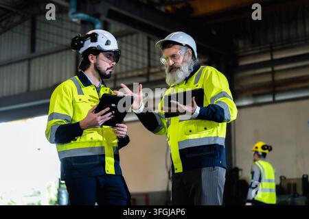 Ingeniero anziano che spiega le operazioni industriali a un collega più giovane in uno stabilimento di produzione. Concetto di leadership ingegneristica aziendale, Corporat Foto Stock
