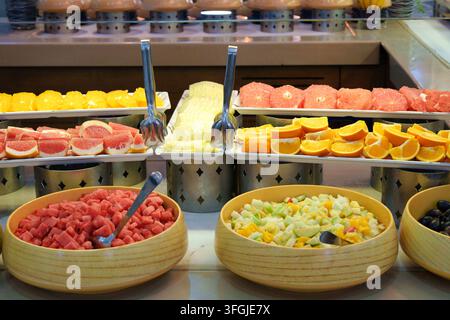 Una vasta selezione di frutta fresca su un buffet della colazione in hotel con arance affettate, pompelmo, melone, anguria a cubetti in ciotole di legno e frutta Foto Stock