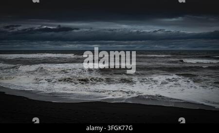 Le onde si infrangono contro la riva vulcanica nera di Khalaktyrsky Beach a Kamchatka, sotto un cielo tempestoso sulla costa più orientale della Russia. Foto Stock