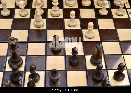 Prima piano dettagliata di una scacchiera di legno con pedine scure e chiare a metà partita, concentrandosi sul posizionamento tattico e sulla strategia all'aperto. Foto Stock