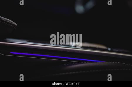 Prima di una console centrale moderna dell'interno dell'auto con illuminazione a LED ambientale viola luminosa in una cabina buia di notte. Foto Stock