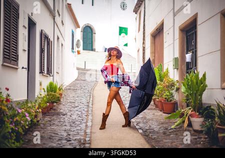 Una donna elegante che tiene un ombrello aperto mentre cammina lungo un vicolo tradizionale lastricato con case imbiancate a calce a Cachopo Foto Stock