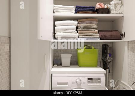 Lavatrice bianca sotto scaffali aperti con asciugamani ordinatamente piegati. Foto Stock