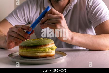 Uomo che prepara un’iniezione di insulina con un dolce donut sul tavolo, perdita di peso e gestione del diabete. Ozempic GLP-1 perdita di peso, Tirzepatide, snellimento, cibo Foto Stock