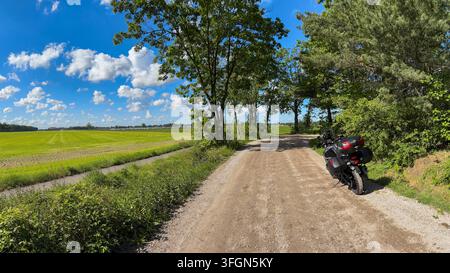 Una strada sterrata che attraversa un paesaggio rurale con una moto parcheggiata sul lato destro. Foto Stock