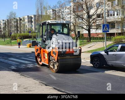 Un compattatore stradale della marca HAMM con colorazione arancione e grigia sta posando asfalto fresco su una strada urbana. Il macchinario pesante è posizionato su Foto Stock