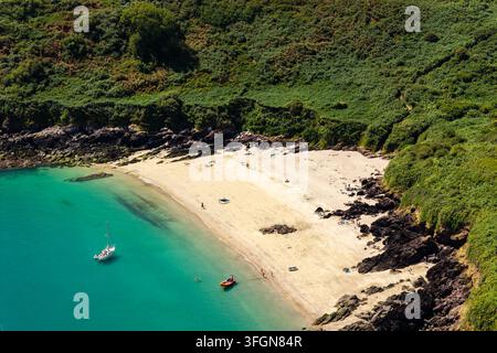 Vista aerea ad alta angolazione di una baia sabbiosa isolata circondata da ripide pendici ricoperte di vegetazione, acqua smeraldina limpida con piccole barche ancorate vicino alla riva in estate Foto Stock