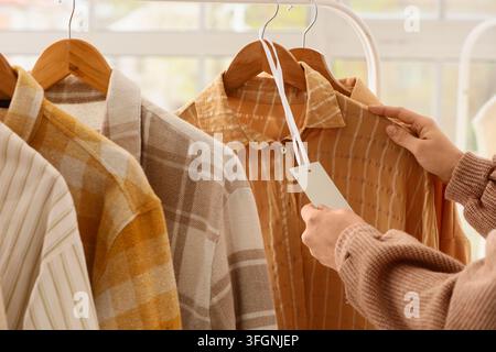 Moda sostenibile e consumo consapevole, persona che controlla l’etichetta del prezzo su una camicia a quadri gialla in un negozio di abbigliamento con scelte di abbigliamento ecologiche Foto Stock