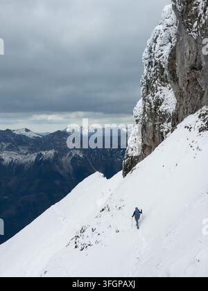 Alpinista che scende un ripido pendio innevato accanto a una scogliera rocciosa sulla vetta del monte Reichenstein durante una spedizione di arrampicata invernale ad alta quota a Eis Foto Stock