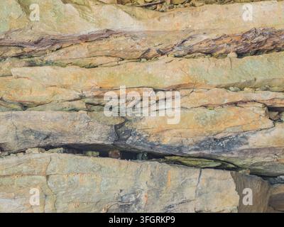Prima vista di un muro di roccia strutturato con strati orizzontali di pietra gialla, marrone e grigia con una piccola fessura scura Foto Stock