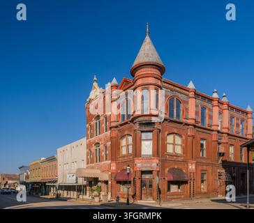 Arkansas, Stati Uniti, 05 SET 2026 - Un grande edificio commerciale in mattoni rossi con una torretta angolare e finestre ad arco si erge in una strada tranquilla Foto Stock
