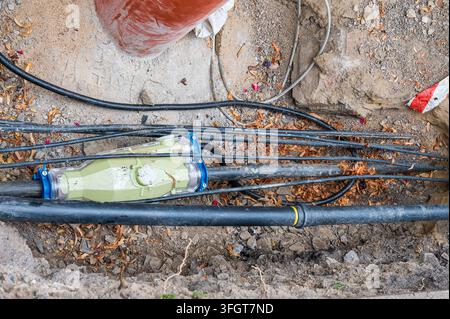 Cavi elettrici sotterranei e manicotto di giunzione in resina in una trincea di servizio scavata. Foto Stock