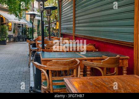 Terrazza ristorante all'aperto vuota con tavoli e sedie in legno tradizionali su strada pedonale ad Atene, Grecia. Attività alberghiera, mediterranea Foto Stock