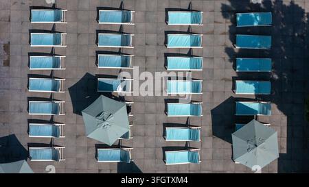 Vista aerea di file di sedie a sdraio blu e ombrelloni disposti su un deck piscina lastricato all'aeroporto internazionale di Los Angeles. Los Angeles, California, U Foto Stock