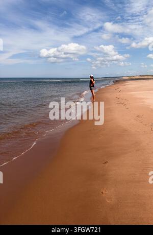 Donna in piedi da sola su una vasta spiaggia sabbiosa mentre guarda l'oceano Foto Stock