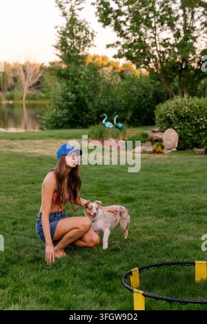Giovane donna che accarezza un cucciolo di Australian Shepherd all'aperto Foto Stock
