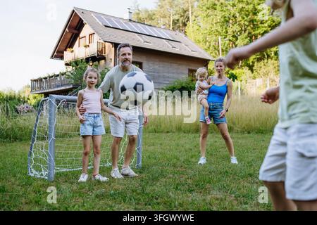 Famiglia che gioca a calcio insieme nel cortile sul retro durante l'estate. Foto Stock