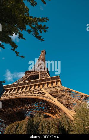 Torre Eiffel, un famoso punto di riferimento a Parigi, in Francia, che si erge contro un cielo blu terso, visto da un angolo basso con alberi circostanti Foto Stock