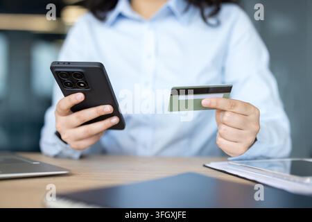 Shopping online e pagamento digitale, donna che utilizza smartphone e carta di credito per una transazione finanziaria alla scrivania dell'ufficio. Dipendente professionista impegnata nei processi di acquisto e bancari nel commercio elettronico. Foto Stock