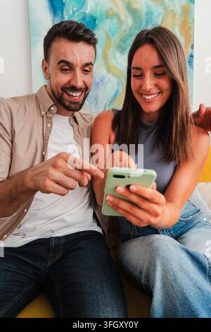 Due persone condividono un momento leggero mentre visualizzano contenuti su un dispositivo portatile, gli occhi brillano e i sorrisi sono ampi. L'immagine trasmette una connessione amichevole Foto Stock