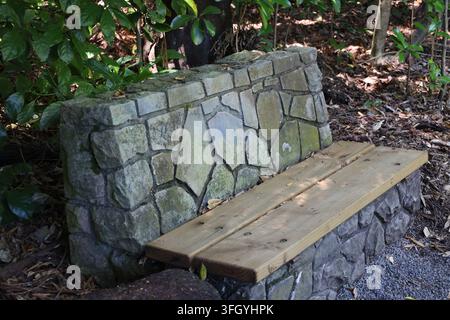 panca in muro di pietra rustica, sedile in legno naturale lungo un vialetto di ghiaia davanti a una foresta fitta, fogliame (primo piano, foresta pluviale, tropicale) Foto Stock