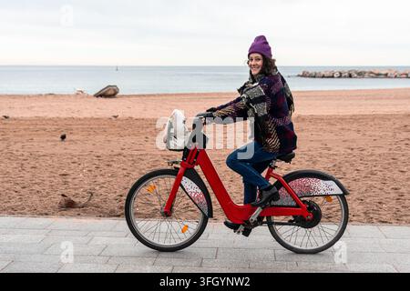 Donna sorridente in sella a una bicicletta rossa sulla passeggiata sul mare Foto Stock