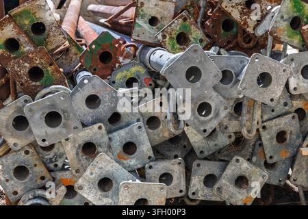 Vista ravvicinata di piastre di base di impalcature arrugginite impilate che mostrano metallo stagionato, corrosione sfogliata e fori geometrici ripetitivi. Adatto per l'industria Foto Stock