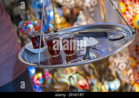 Vista di una persona che porta un vassoio tradizionale in metallo con bicchieri di tè turco e zuccherini in un vivace bazar a Istanbul, Istanbul, Turchia. Foto Stock