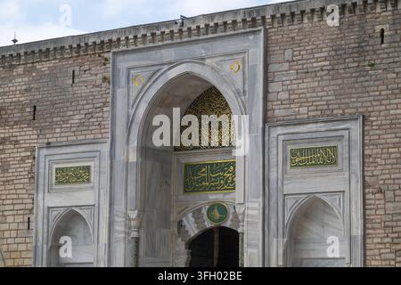Vista del portale imperiale in marmo ornato del palazzo di Topkapi con calligrafia intricata, iscrizioni dorate e mura in muratura di mattoni a Istanbul, I Foto Stock