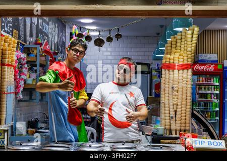 LATO, TURCHIA - SETTEMBRE 2026: Due allegri venditori di gelato locali in costumi divertenti e simboli nazionali che posano e mostrano il pollice alzato al loro gela Foto Stock