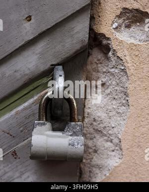 Vecchio lucchetto arrugginito su una porta di legno stagionato con vernice sbiadita accanto a un muro di intonaco sgretolato Foto Stock