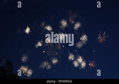Uno splendido spettacolo pirotecnico con numerose piccole esplosioni che spargono nuvole di scintille bianche brillanti nel cielo notturno. Foto Stock