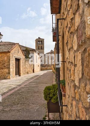 Via acciottolata storica con campanile - Un'incantevole vecchia via acciottolata si snoda attraverso un villaggio spagnolo storico, fiancheggiata da edifici tradizionali in pietra Foto Stock