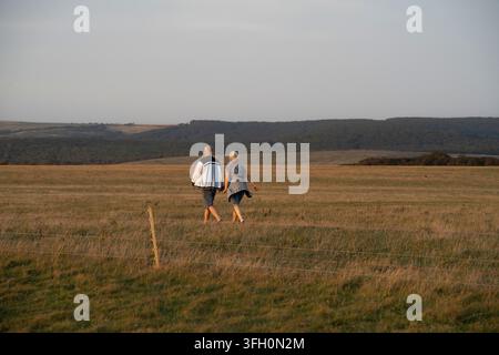Una coppia anziana cammina mano nella mano attraverso un campo erboso del South Downs National Park, in Inghilterra, per godersi il panorama della campagna. Foto Stock