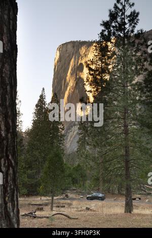 Un SUV scuro è parcheggiato vicino a El Capitan nello Yosemite National Park, CA, per osservare il tramonto che getta una luce dorata sull'iconica scogliera di granito. Foto Stock